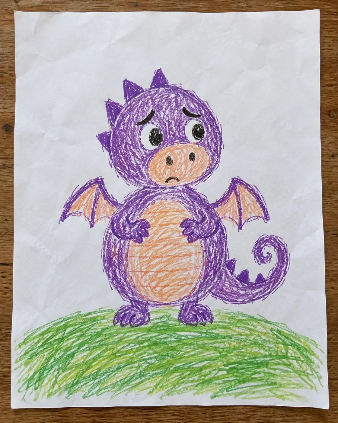 Dibujo infantil con ceras de un pequeño dragón violeta y redondo con cejas preocupadas